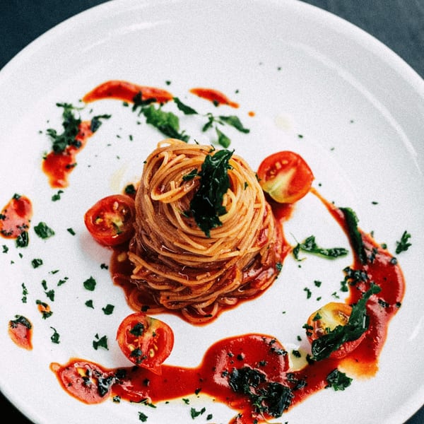 A perfectly plated Italian spaghetti dish with tomato sauce, cherry tomatoes, and fresh herbs.