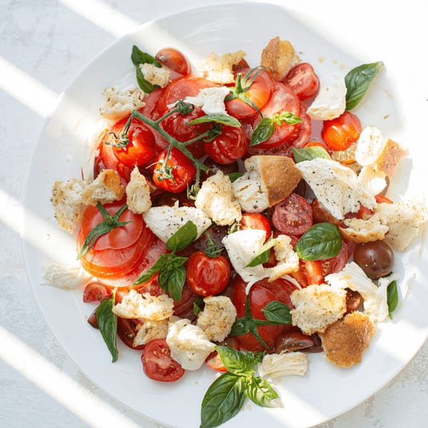 A fresh Italian Panzanella salad with tomatoes, mozzarella, basil, and croutons on a white plate.